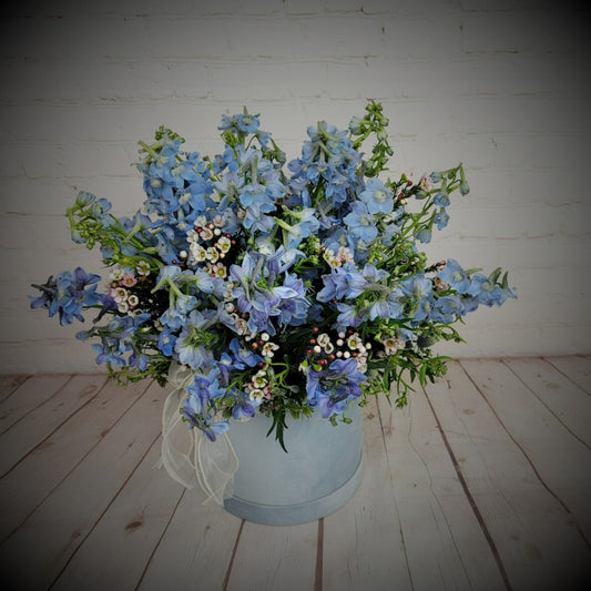 Blue delphiniums and seasonal greenery in blue box